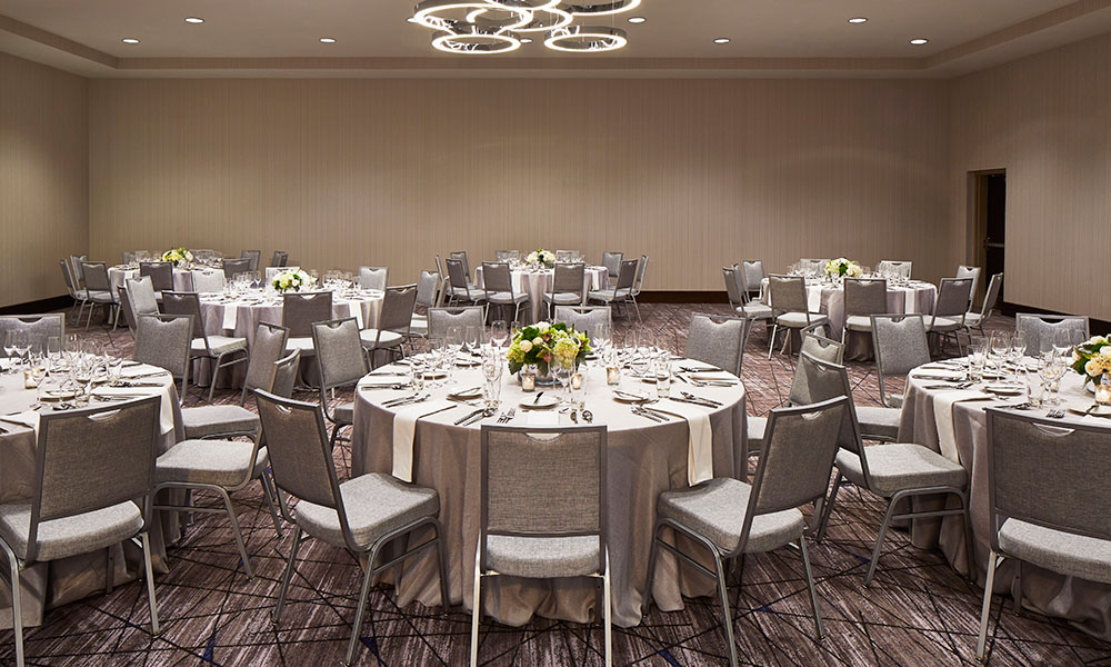 The Ballroom, light brown and gray undertones, set with round tables for a wedding